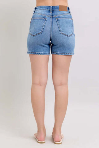 Women's Judy Blue Med Wash Midi Length Classic Denim Shorts on a hanger, showcasing front pockets and a casual, summer-ready design.