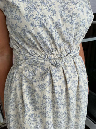 Ivory and blue floral boat neck sleeveless midi dress with pleated design, showcased on a mannequin in a stylish setting.