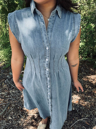 Washed light denim shirt dress with collar, pintuck‑cinched waist and button‑front closure—short sleeves and relaxed midi length