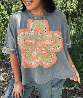 Women's mineral washed blue short sleeve top with vibrant orange flower patch detailing. Perfect for a casual and stylish look.