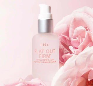 Bottle of FHF - Flat Out Firm® Hyaluronic Acid Peptide Firming Serum on a marble surface with a leafy background.