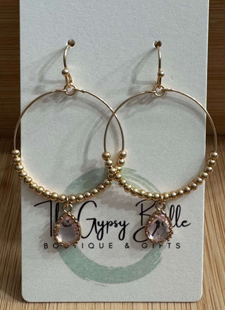 Pink teardrop gold beaded hoop drop earrings on a woven fabric background, featuring intricate detailing and elegant design.