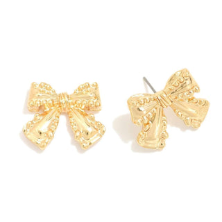 Chunky gold bow post earrings resting on a textured white surface, highlighting their bold and elegant design.