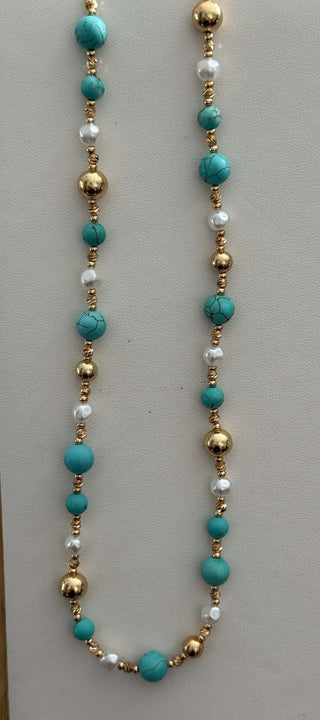 Gold, pearl, and turquoise beaded necklace on a marble surface, showcasing its elegant and vibrant design.