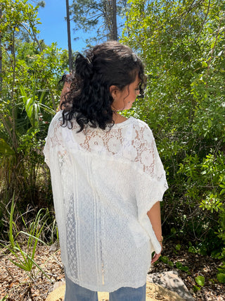 White lace short-sleeve top with intricate floral pattern and handkerchief hem detail.
