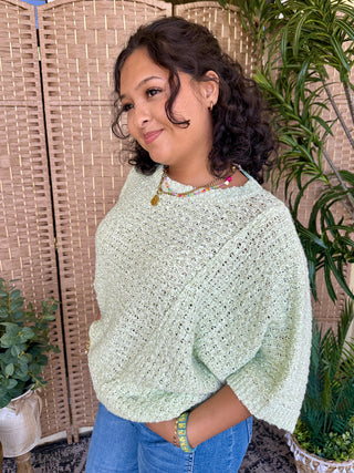 Sage green knit sweater with asymmetrical hem and textured weave pattern.
