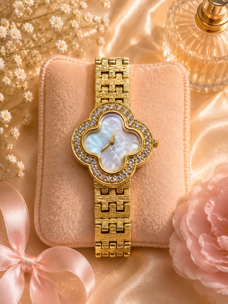 Gold clover watch with mother-of-pearl dial and crystal bezel on velvet blush pouch.

