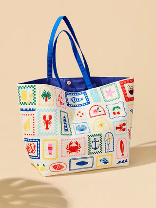 Coastal patchwork tote bag with colorful stamp prints of lobsters, palm trees, crabs, fish, shells, and cherries, featuring bright blue dual handles.
