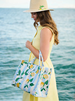 Cream and light blue striped tote with yellow lemon and green leaf pattern, worn by woman at beach.
