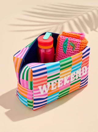 Colorful striped weekend tote bag with rainbow stripes, containing a water bottle and pink mesh pouch.
