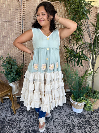 Light blue sleeveless dress with embroidered daisies and tiered cream ruffle skirt.
