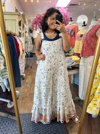 Cream and indigo floral print sleeveless jumpsuit with wide legs and ruffled hem, styled with navy collar trim.
