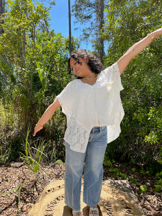 White lace short-sleeve top paired with blue wide-leg jeans, styled outdoors.
