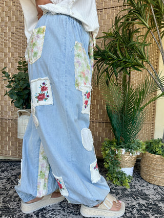 Light blue denim jogger pants with floral patchwork pockets and distressed details.
