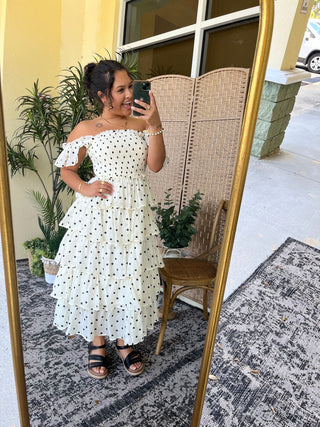 White off-shoulder midi dress with black polka dots and ruffled sleeves.
