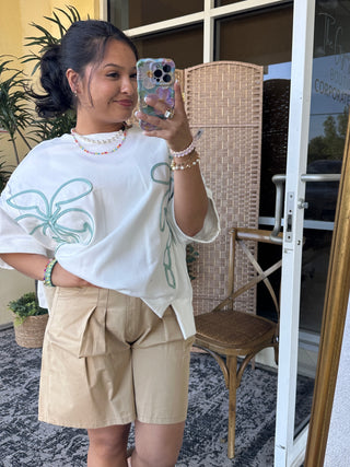 White oversized tee with turquoise palm tree graphic and side seam details.
