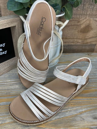 White strappy wedge sandal with cork sole and tan footbed, displayed from top and side view.
