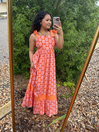 Orange maxi dress with white geometric print, ruffle neckline, and tiered skirt detail.
