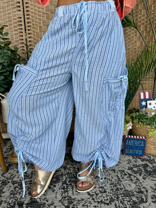 Blue pinstripe parachute pants with drawstring cuffs and side cargo pockets.
