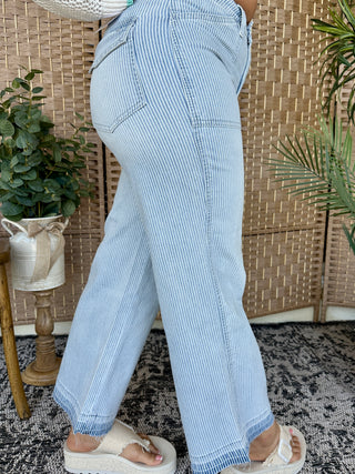 Light blue and white vertical striped jeans with raw frayed hem and five-pocket styling.
