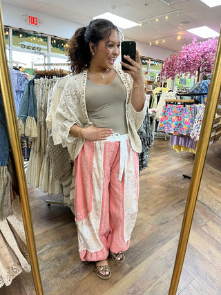 Cream crochet shrug with short sleeves over gray tank top, paired with coral and cream patterned pants.
