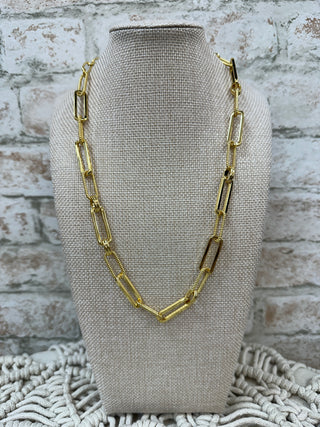 Gold paperclip link chain necklace displayed on beige linen bust form.
