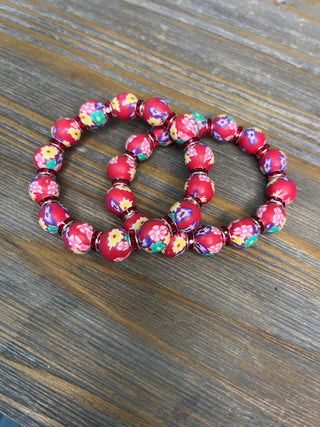 Red boho stretch clay bead bracelets with colorful floral pattern details on wooden surface.
