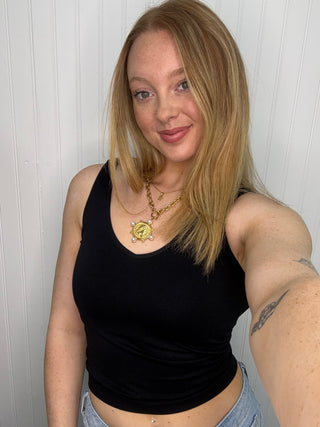 Black seamless tank top with scoop neckline worn with gold pendant necklace.
