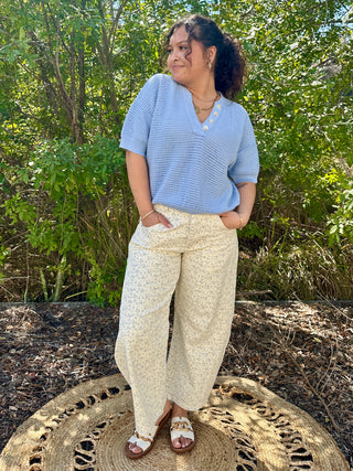 Sky blue textured v-neck short sleeve top with pearl button detail paired with cream floral pants.

