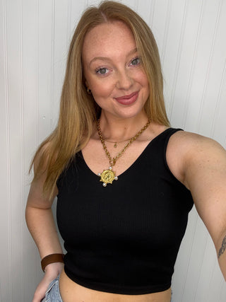 Black ribbed seamless tank top with deep V-neckline styled with gold chain necklace.
