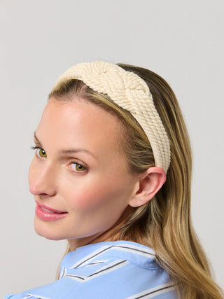 Cream cable knit headband twisted at center, worn on blonde hair.
