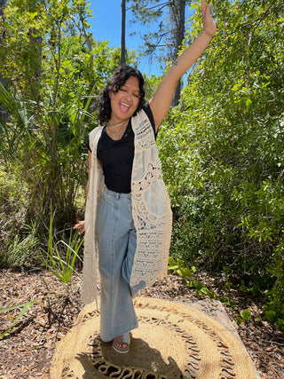 Cream crochet vest with openwork pattern over black tank top and light blue jeans.
