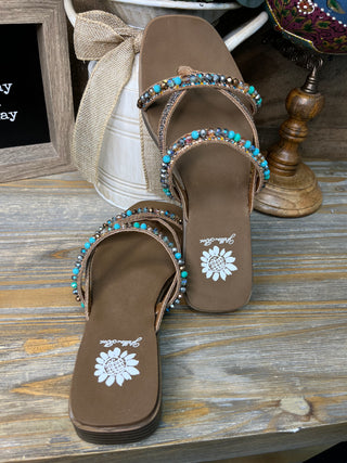 Brown leather sandals with turquoise and rhinestone embellished straps and white sunflower sole design.
