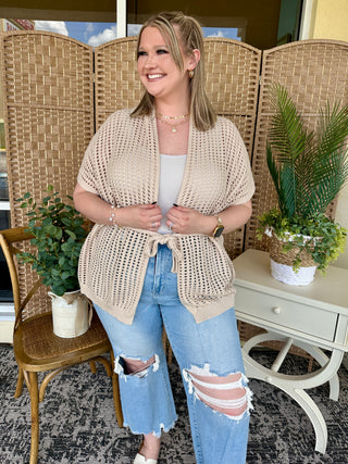 Beige open weave short-sleeve cardigan worn over white tank top with distressed blue jeans.
