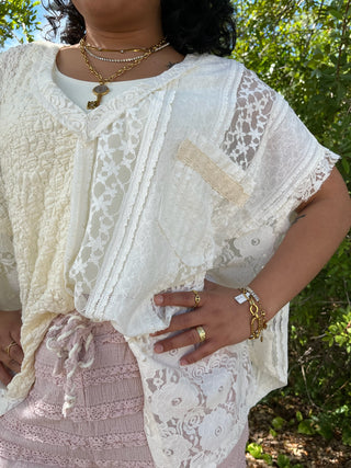 Ivory lace short-sleeve top with mixed floral and geometric patterns and handkerchief hem detail.
