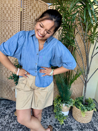 Blue chambray button-up shirt with puffed sleeves, worn with cream shorts.
