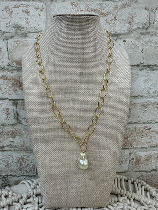 Gold chain necklace with baroque pearl drop pendant on cream linen bust form display.
