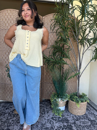 Cream waffle-knit sleeveless henley tank top with button placket and wavy hem detail.
