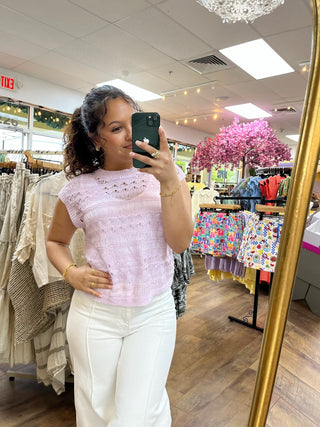 Lilac crochet sleeveless top with textured knit pattern paired with white pants.
