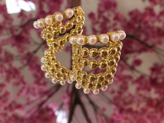 Gold beaded hoop earrings with triple pearl accents on floral background.
