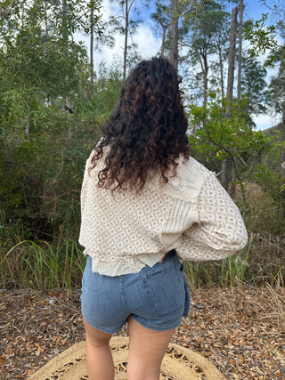 Ivory floral jacket with textured knit detail and ruffled hem, styled with blue denim shorts.
