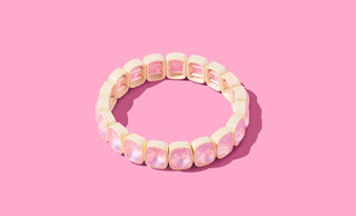 Cream and gold beaded stretch bracelet with pink iridescent stone accents on pink background.