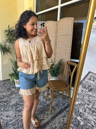 Cream lace sleeveless top with ruffled hem paired with medium-wash denim shorts.
