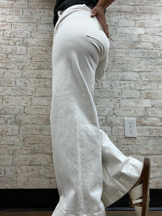 White wide-leg jeans with relaxed fit and cuffed ankles, shown from side view against brick wall.
