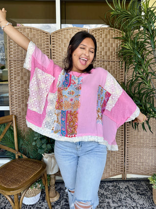 Candy pink oversized top with colorful floral patchwork panels and white textured trim, worn with light blue jeans.
