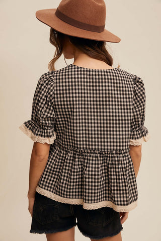 Person wearing a checkered blouse with ruffled sleeves and a brown hat on a beige background