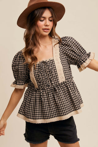 Woman wearing a checkered blouse with lace trim and a brown hat on a beige background