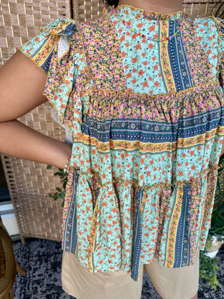 Sage floral patchwork top with ruffled short sleeves and tiered hem in multi-colored print.
