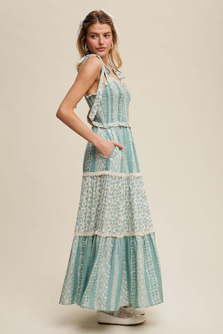 Woman wearing a sage floral Listicle Maxi Dress with smock tiers and ruffle details, standing in a sunlit garden.