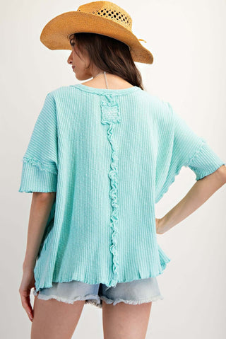 Women's oversized ribbed texture top with short sleeves, available in two colors, displayed on a wooden easel background.